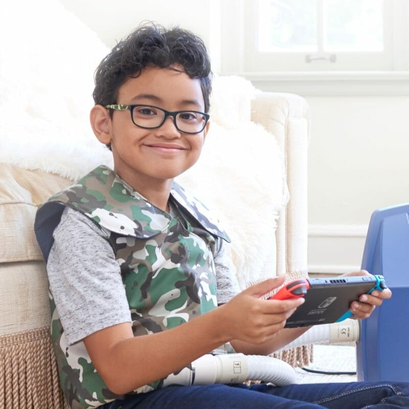 A pediatric SmartVest Airway Clearance System patient plays video games and relaxes while using his SmartVest.