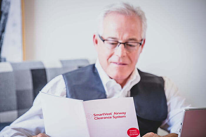 Older man wearing The SmartVest Airway Clearance System while reading brochure on its benefits.