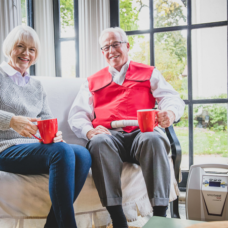 An older couple sits on their sofa while drinking coffee together