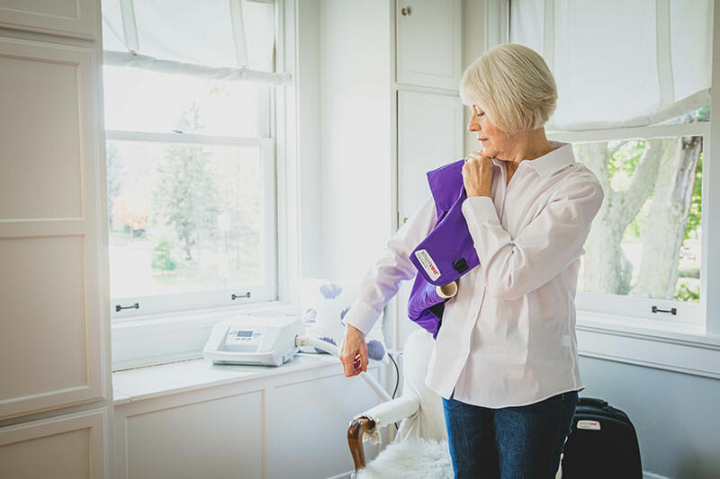Older woman putting right arm into purple SmartVest at home.