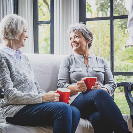 Two older women drinking coffee on a couch together