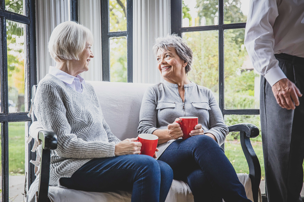 A couple of older women having a cup of coffee together on the couch