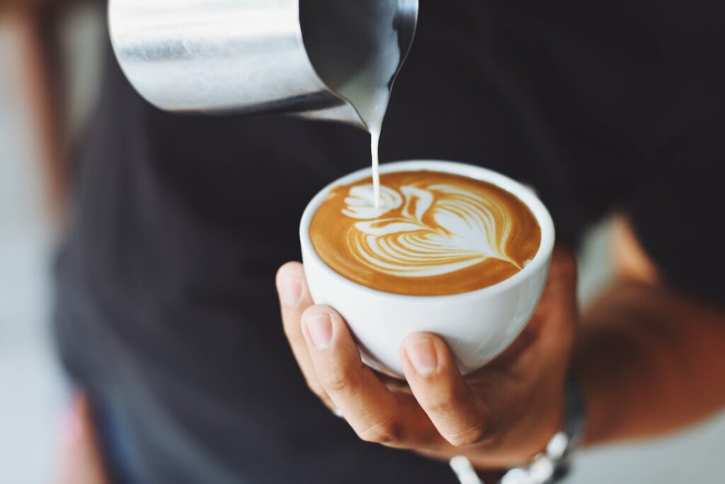 A barista pouring froth into latte cup to make a design.