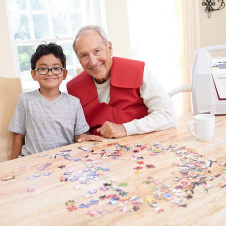 An older man wearing a SmartVest works on a puzzle with a boy