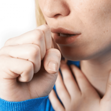 A person holds their chest as they cough into their fist