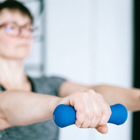 A woman holds out 1 lb weights with straight arms