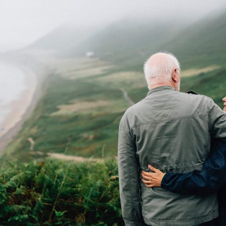 An older couple embraces on a rural hilltop