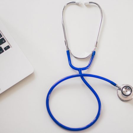 A stethoscope rests on a table near a laptop