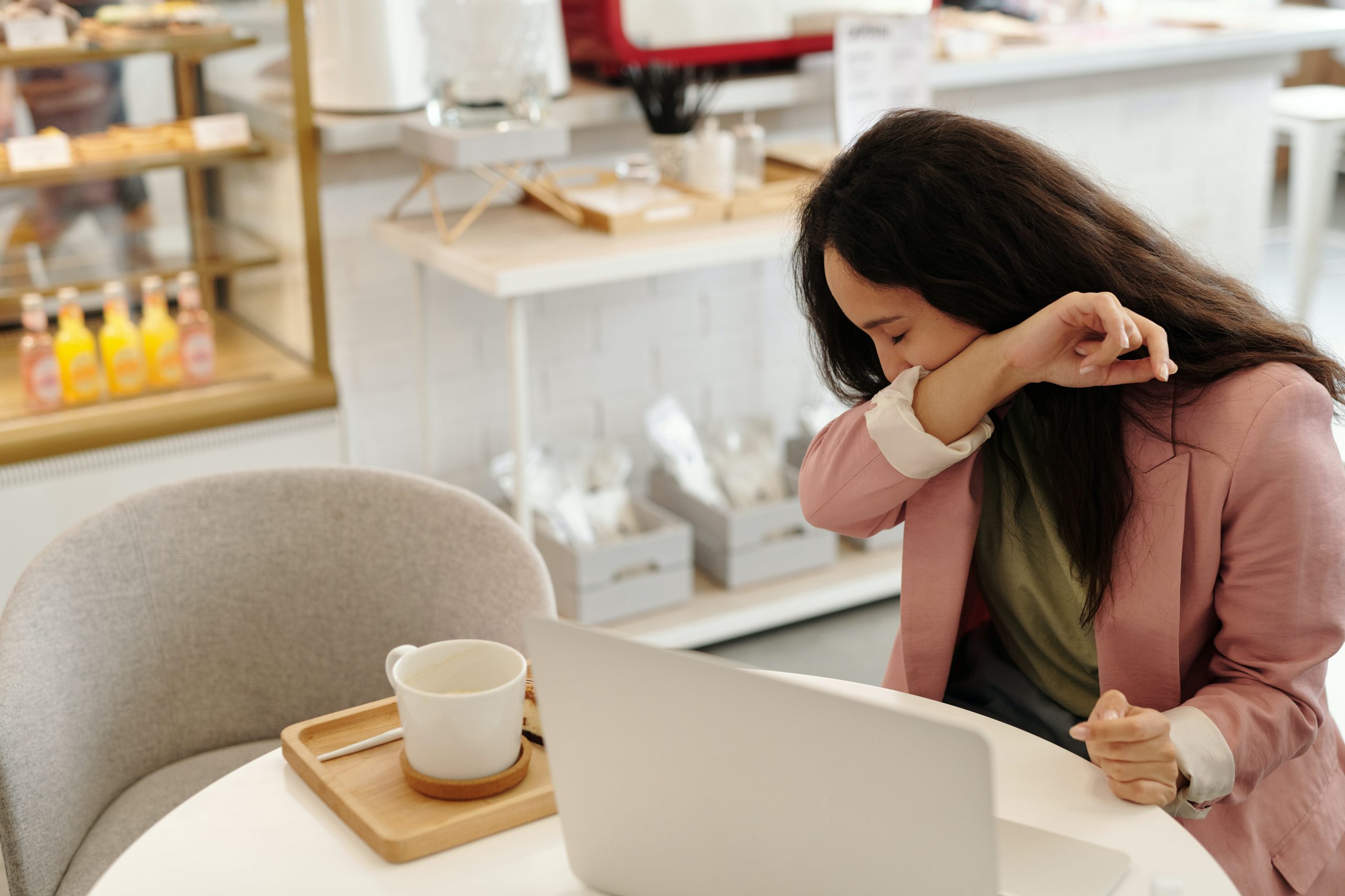 Woman coughing into elbow while sitting at cafe table in restaurant.