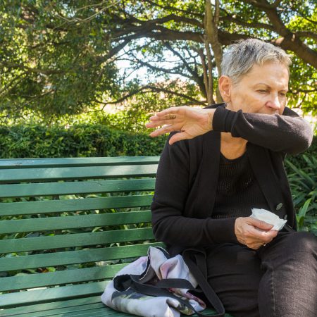 A woman coughs into her elbow while outdoors