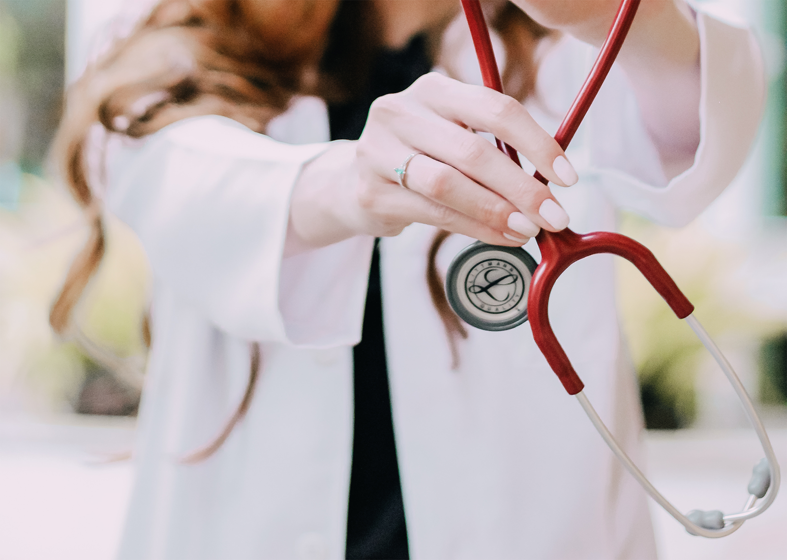 Red headed female doctor holding a red stethoscope in hand.