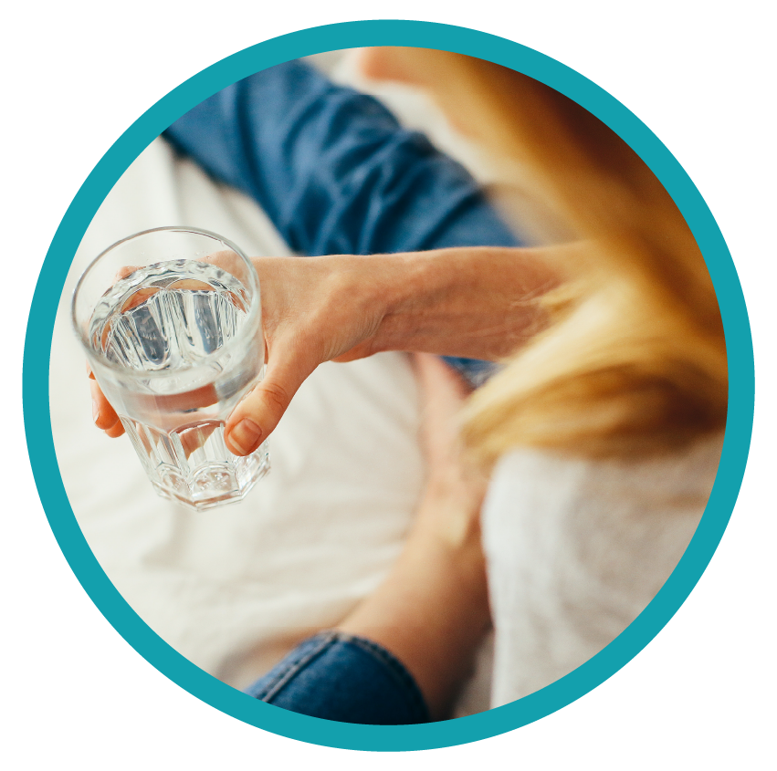 Woman sitting on bed holding a glass of water.