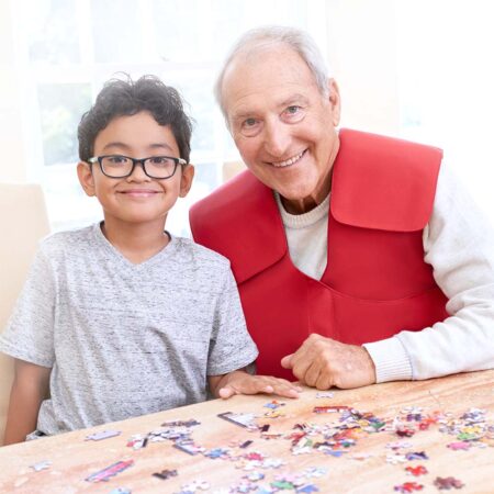 An old man wearing his SmartVest works on a puzzle with a kid