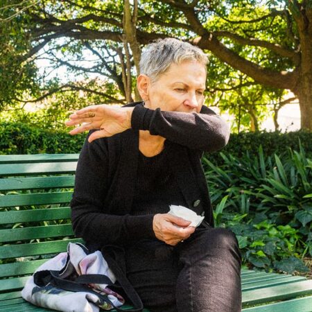 A woman coughing into her arm on a bench in the park