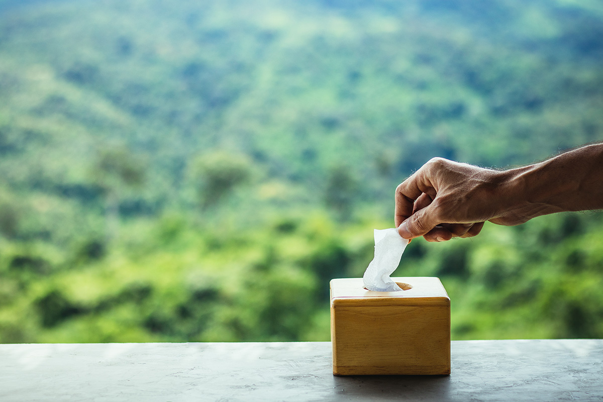 Man's hand grabbing tissue paper from box on wooden table with blur natural mountain view background.